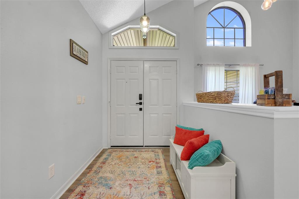 A bright entryway features double doors, a vaulted ceiling, a patterned rug, and a bench — 305 FORREST CREST COURT, OCOEE, FL
