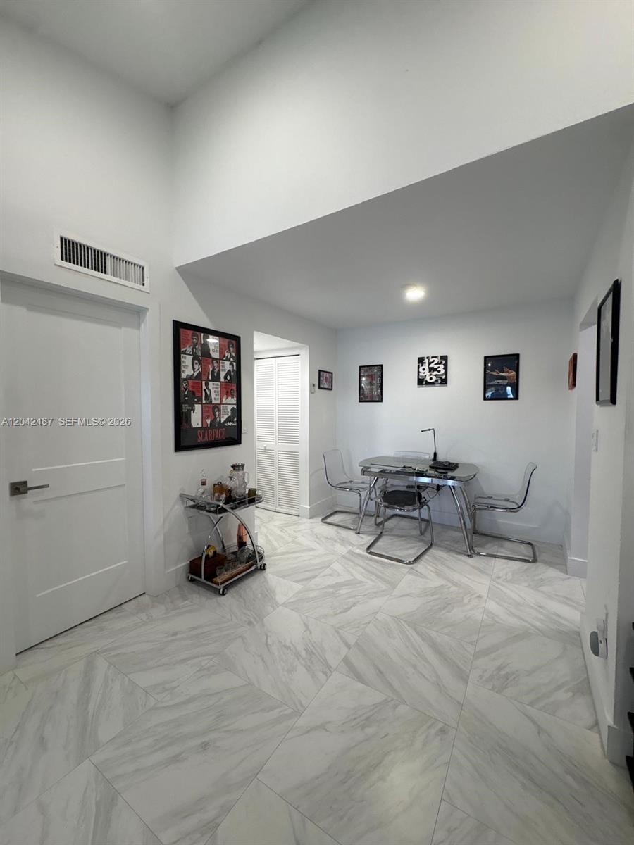 A dining area features white marble-look tile flooring, a glass table, and framed wall art — 15560 SW 80th St # 205, Miami FL 33193, MIAMI, FL