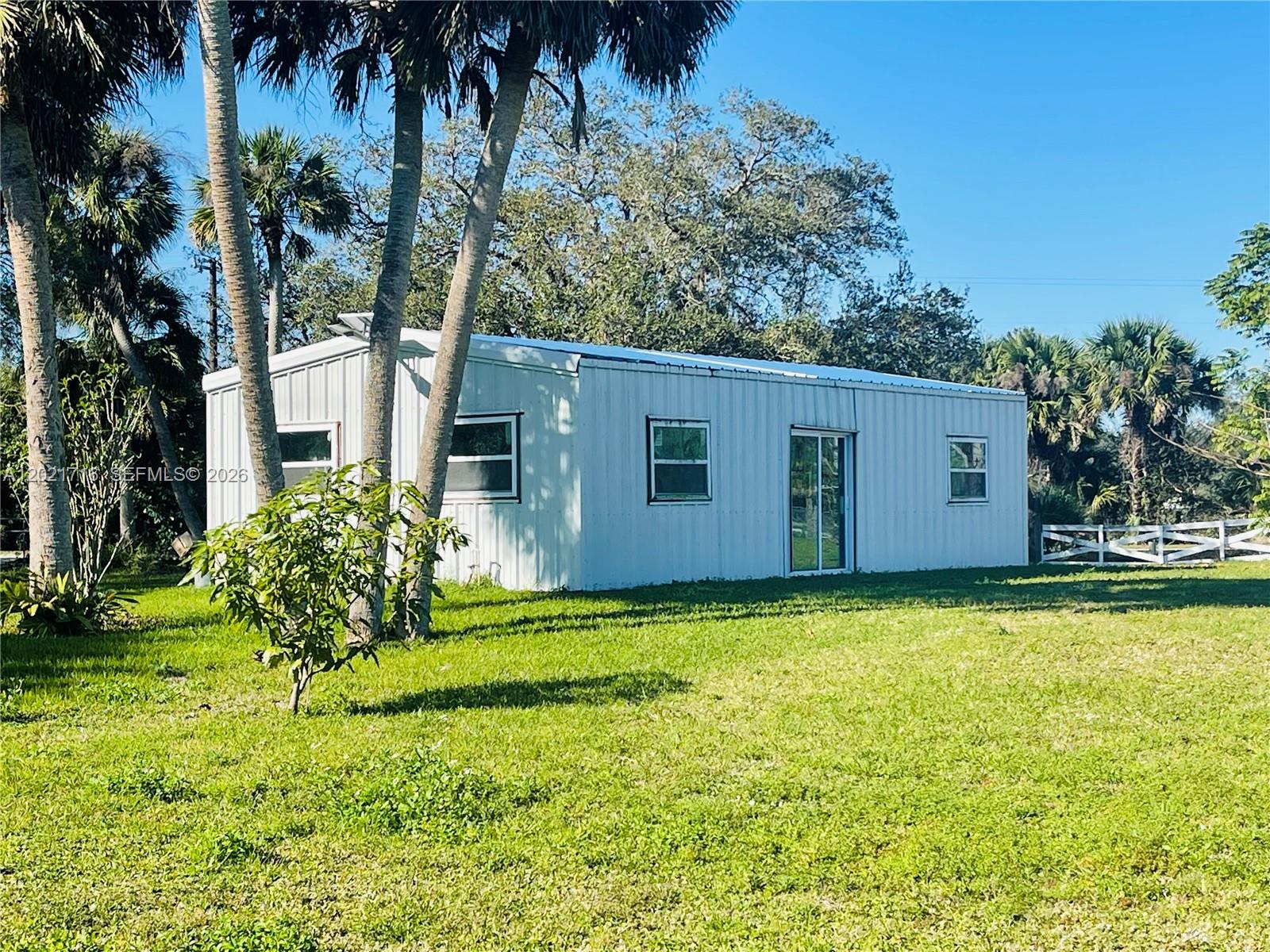 A white metal-sided rectangular building sits on a grassy lawn surrounded by palm trees — 1326 Red Barn Rd, Moore Haven FL 33471, MOORE HAVEN, FL