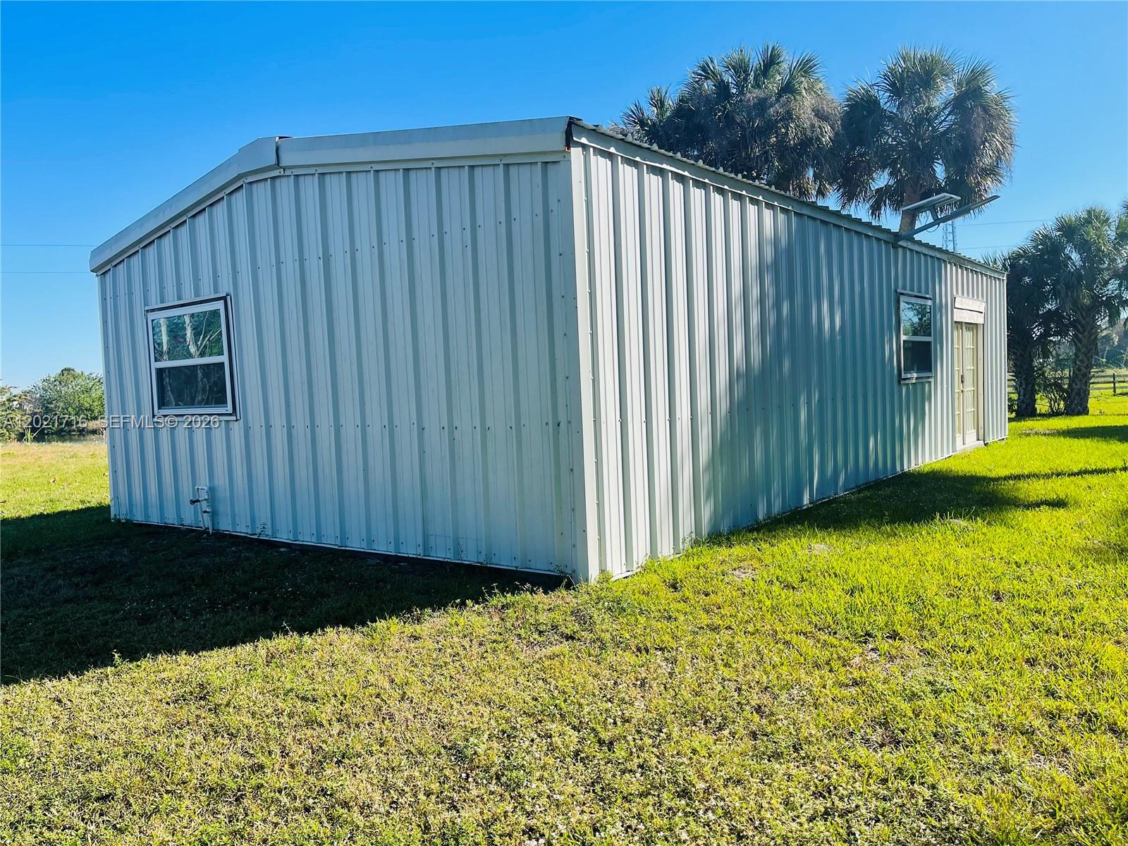 A metal-sided structure with a gabled roof sits on a grassy lot with palm trees — 1326 Red Barn Rd, Moore Haven FL 33471, MOORE HAVEN, FL