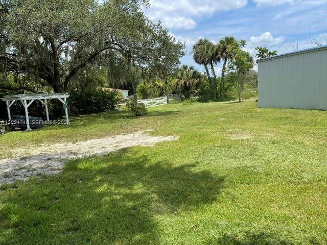 A grassy yard features a white pergola, a metal building, and mature trees — 1326 Red Barn Rd, Moore Haven FL 33471, MOORE HAVEN, FL