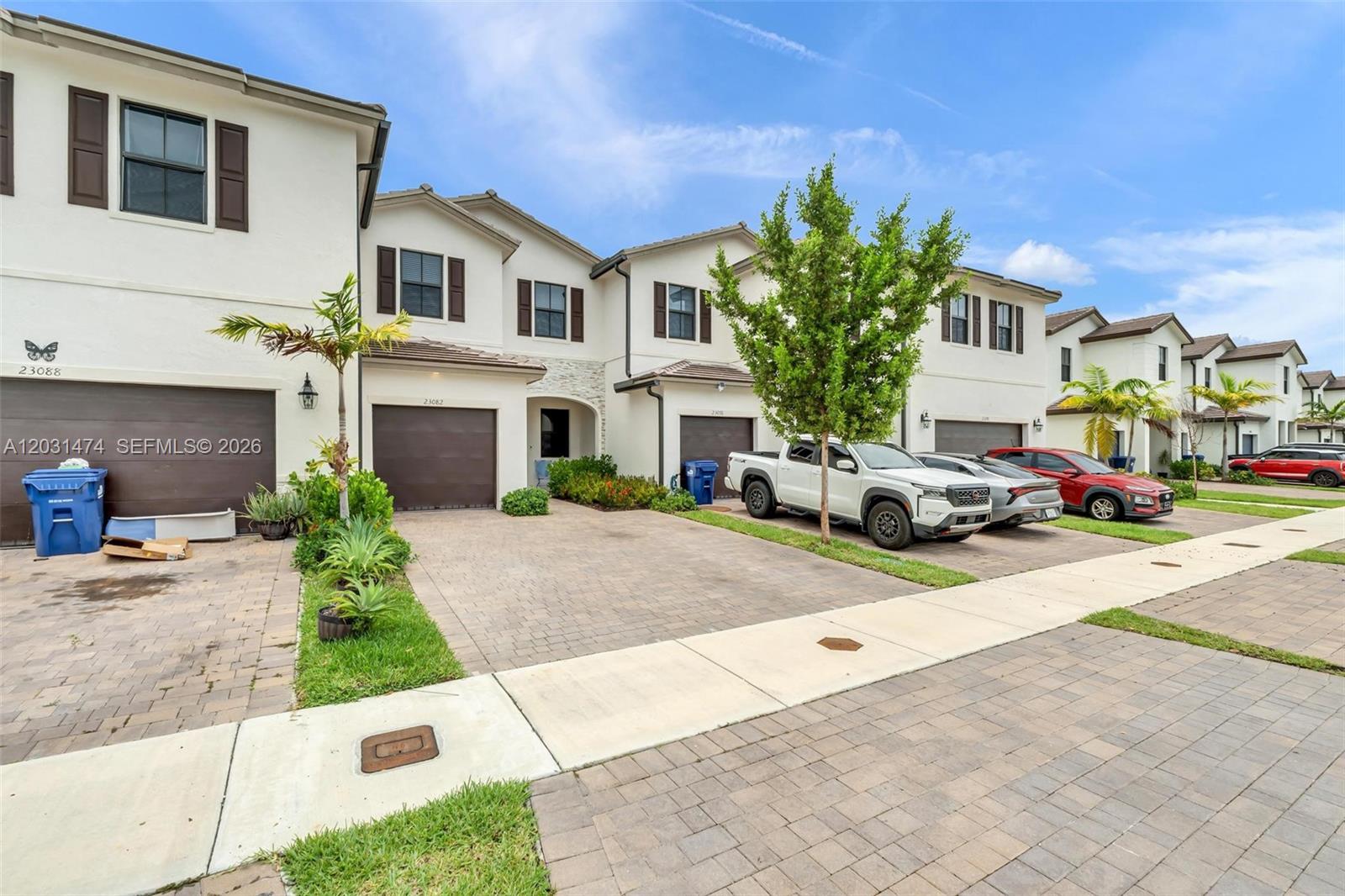A row of multi-story townhomes features paved driveways, attached garages, and parked vehicles — 23082 SW 129th Ct, Miami FL 33170, MIAMI, FL
