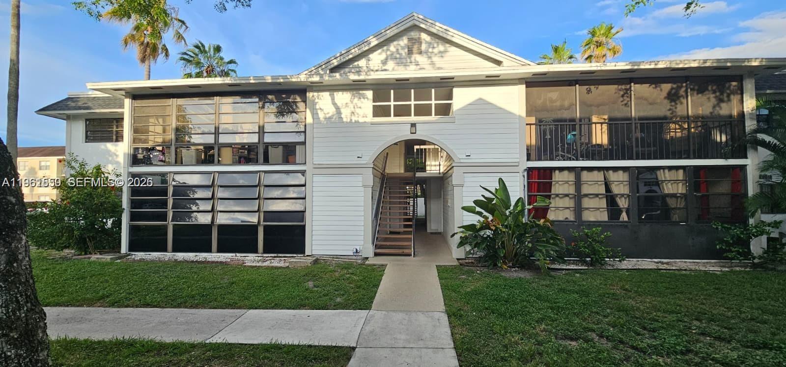 A two-story residential building features a central arched entryway with stairs and screened-in balconies — 18965 NW 62nd Ave # 202, Hialeah FL 33015, HIALEAH, FL