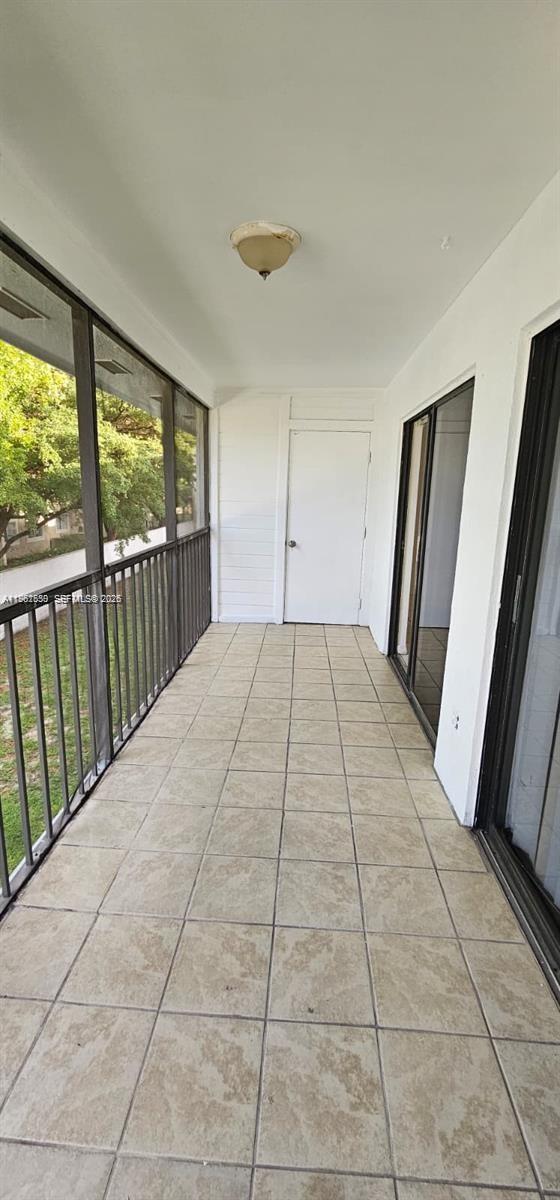 A screened-in balcony features beige tile flooring, a white door, and a metal railing — 18965 NW 62nd Ave # 202, Hialeah FL 33015, HIALEAH, FL