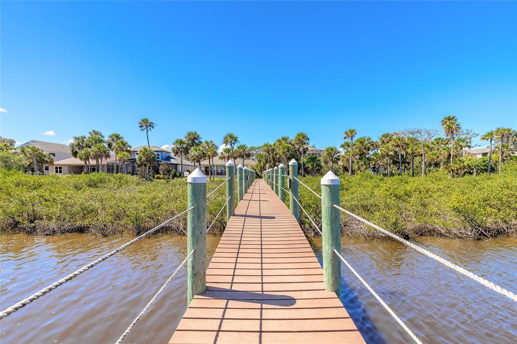 A wooden boardwalk leads through mangroves toward houses under a clear blue sky — 31 S RIVERWALK DRIVE, PALM COAST, FL