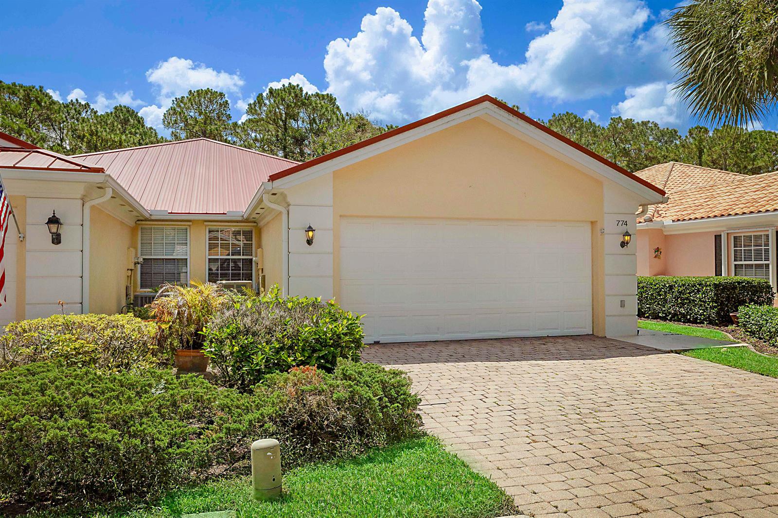 A single-story house with a white garage door, tan stucco walls, and a metal roof — 774 SW Balmoral Trace, Stuart FL 34997, STUART, FL
