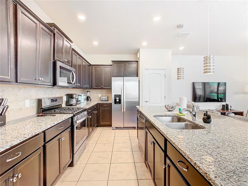 A kitchen features dark wood cabinetry, granite countertops, stainless steel appliances, and tile flooring — 4594 TERRASONESTA DRIVE, DAVENPORT, FL