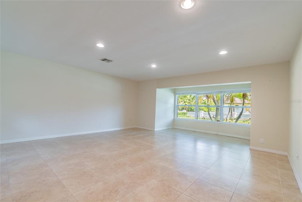 An empty room with beige tile flooring, recessed lighting, and a large windowed alcove — 303 WILDWOOD WAY UNIT A, CLEARWATER, FL