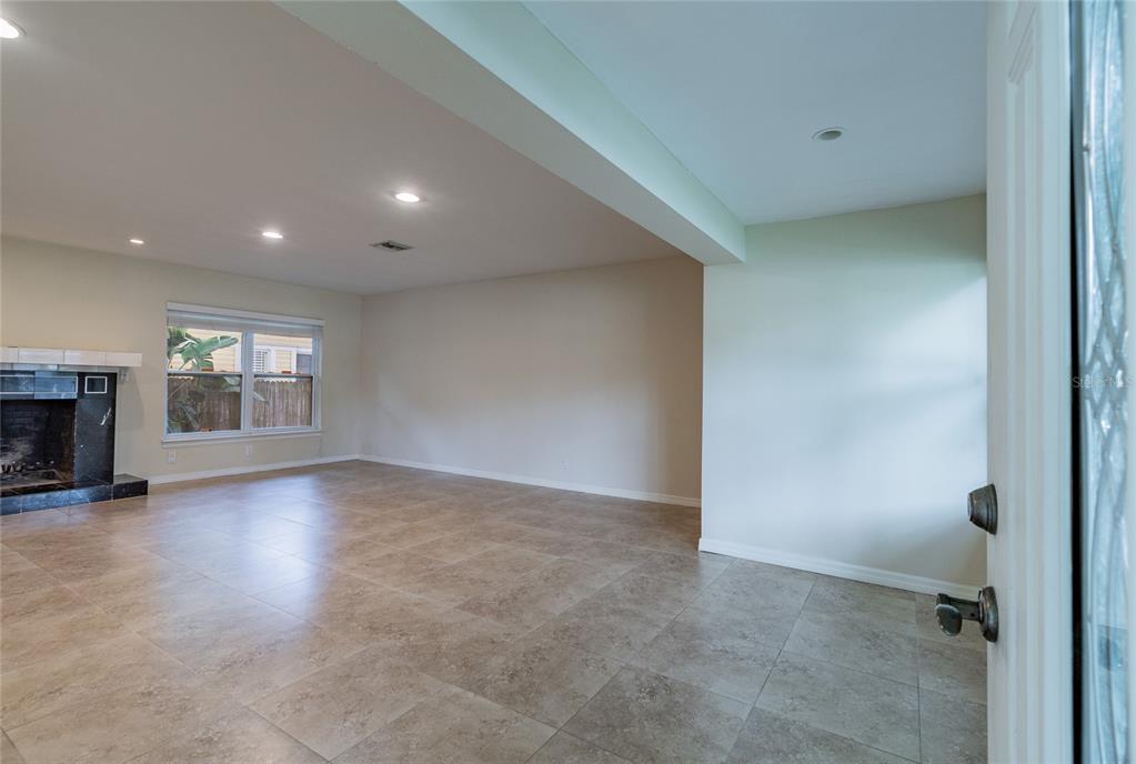An empty living room features large beige floor tiles, a fireplace, and recessed lighting — 303 WILDWOOD WAY UNIT A, CLEARWATER, FL