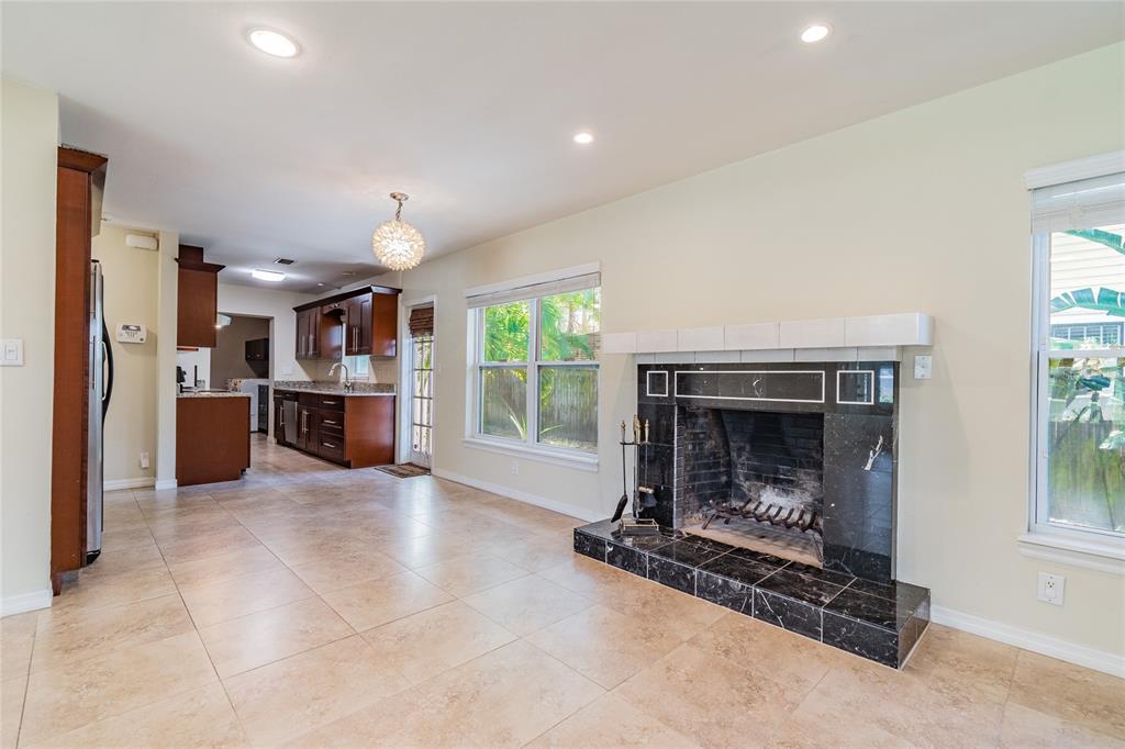 A living room with tile flooring and a black marble fireplace connects to a kitchen — 303 WILDWOOD WAY UNIT A, CLEARWATER, FL