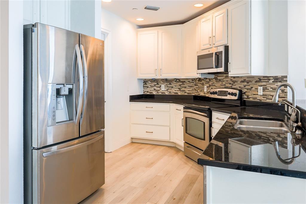 A kitchen with white cabinets, stainless steel appliances, black countertops, and light wood flooring — 449 S 12TH STREET UNIT 1101, TAMPA, FL
