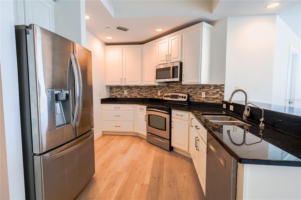 A kitchen features white cabinets, black countertops, stainless steel appliances, and light wood flooring — 449 S 12TH STREET UNIT 1101, TAMPA, FL