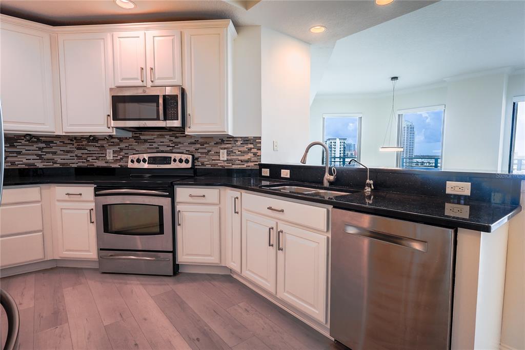 A kitchen with white cabinets, stainless steel appliances, black countertops, and a view of buildings — 449 S 12TH STREET UNIT 1101, TAMPA, FL