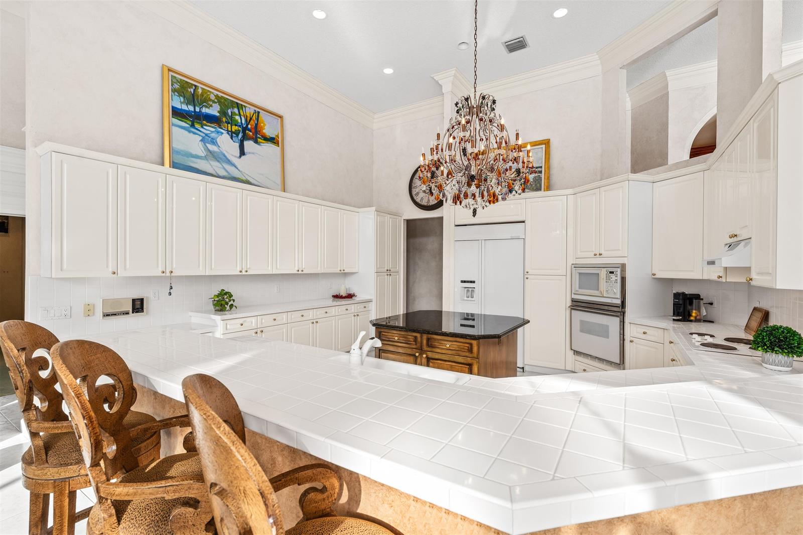 A bright kitchen features white cabinetry, a tiled countertop, a central island, and a chandelier — 4475 NW 24th Terrace, Boca Raton FL 33431, BOCA RATON, FL