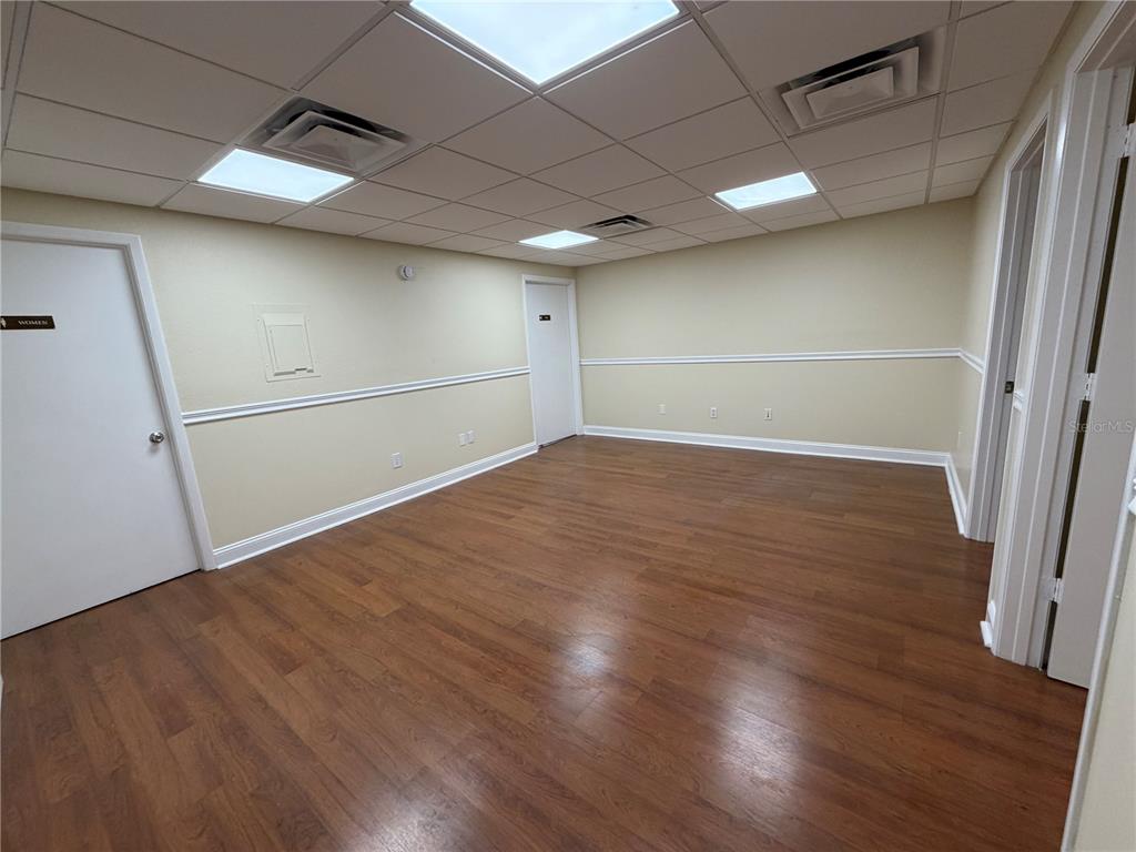 An empty room with wood-look flooring, beige walls, a drop ceiling, and three white doors — 4828 W GANDY BOULEVARD UNIT B27, TAMPA, FL