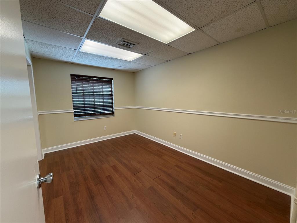 An empty office room with wood-look flooring, beige walls, a window, and drop ceiling lights — 4828 W GANDY BOULEVARD UNIT B27, TAMPA, FL
