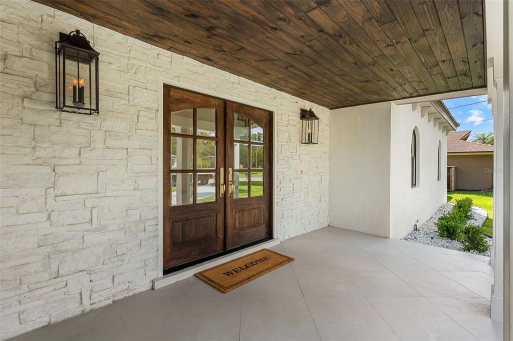 A covered porch features white stone walls, a dark wood ceiling, and double glass doors — 2501 TRENTWOOD BOULEVARD, ORLANDO, FL