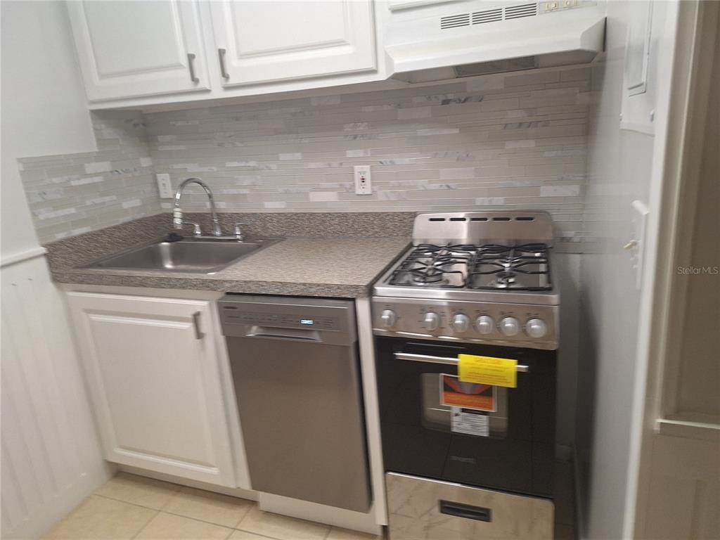 A small kitchen features white cabinets, a stainless steel dishwasher, and a gas range — 136 BLUE POINTE WAY UNIT 350, ALTAMONTE SPRINGS, FL