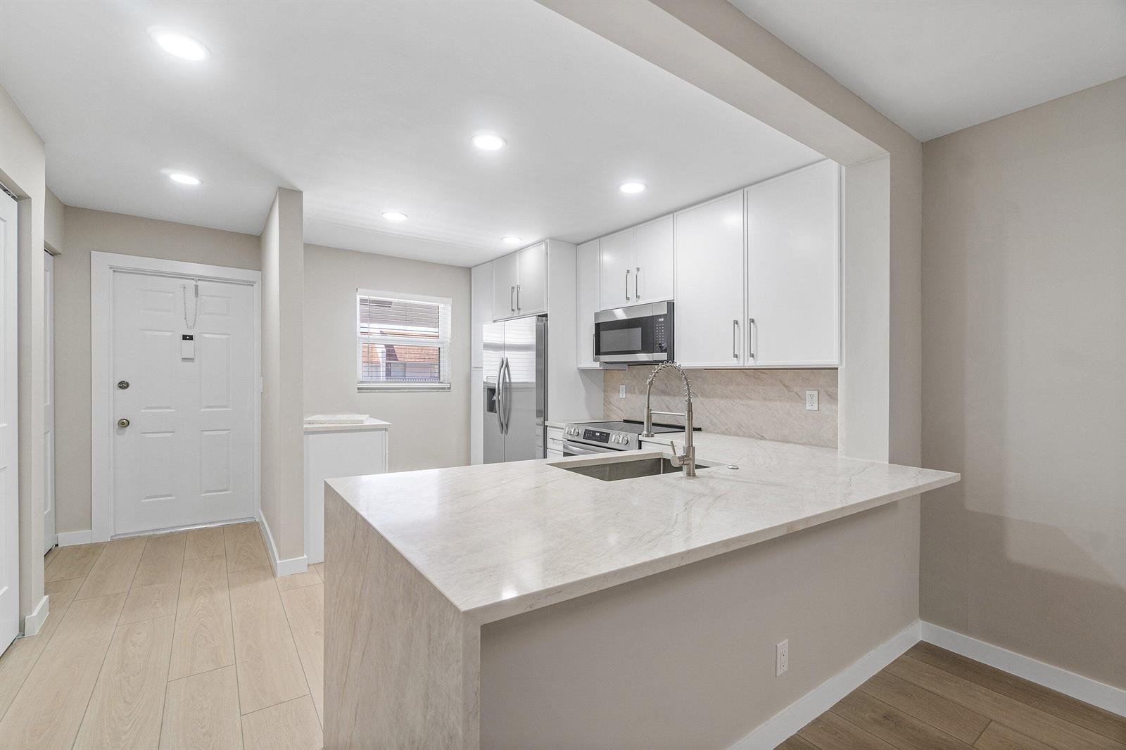 A modern kitchen features white cabinets, stainless steel appliances, and a waterfall edge quartz island — 2905 SW 22nd Avenue # 202, Delray Beach FL 33445, DELRAY BEACH, FL