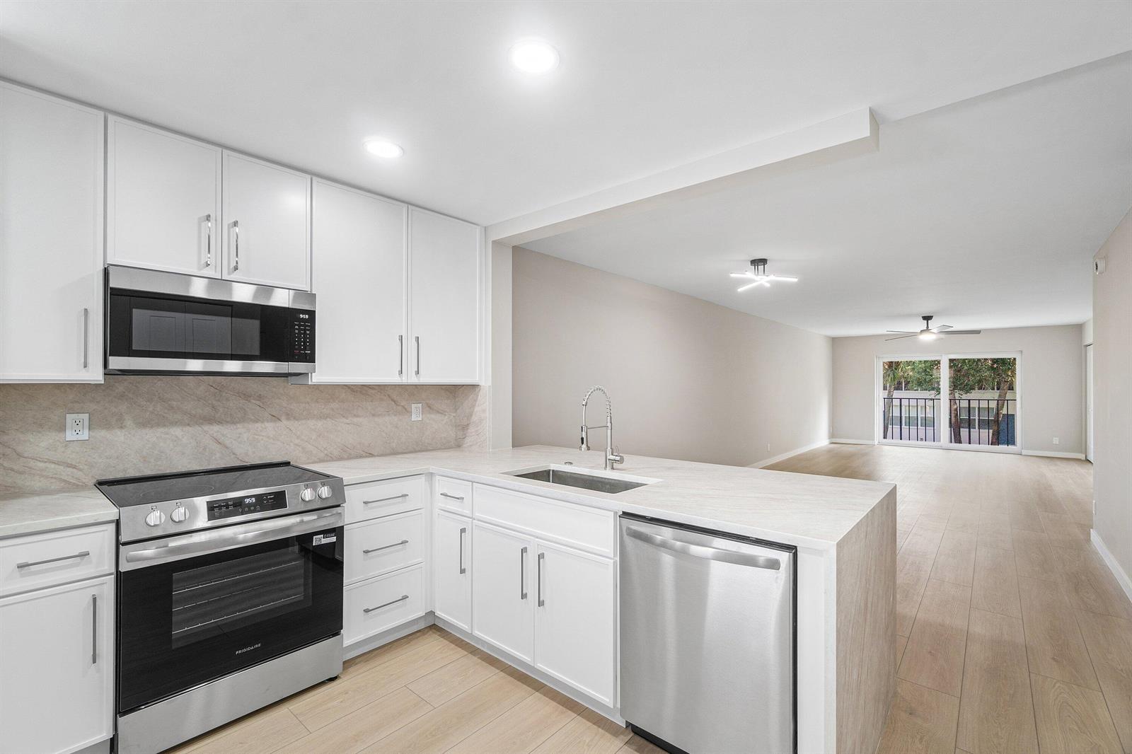 A modern kitchen with white cabinets, stainless steel appliances, and light wood-look flooring — 2905 SW 22nd Avenue # 202, Delray Beach FL 33445, DELRAY BEACH, FL