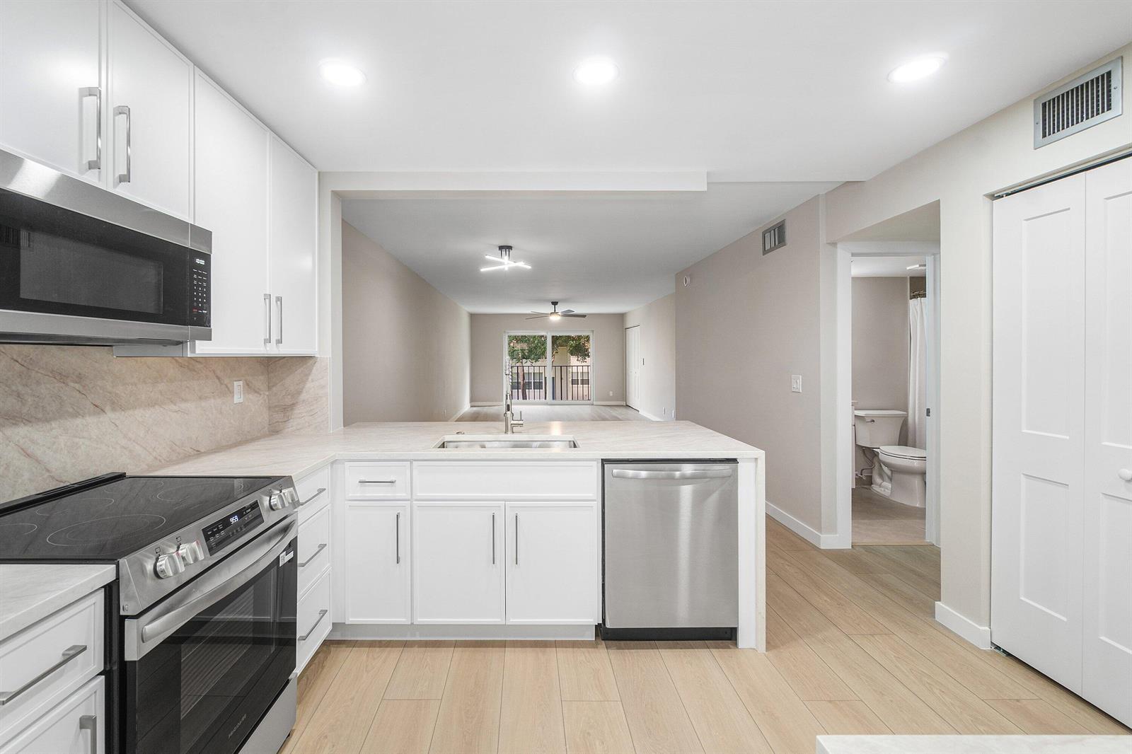 A modern kitchen with white cabinets, stainless steel appliances, and light wood-look flooring — 2905 SW 22nd Avenue # 202, Delray Beach FL 33445, DELRAY BEACH, FL