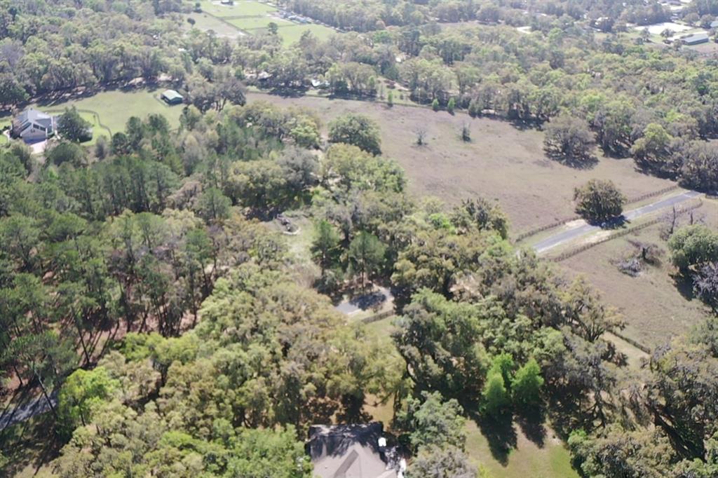 An aerial view shows a house surrounded by dense trees and open grassy fields — 11 SW 144TH COURT, OCALA, FL