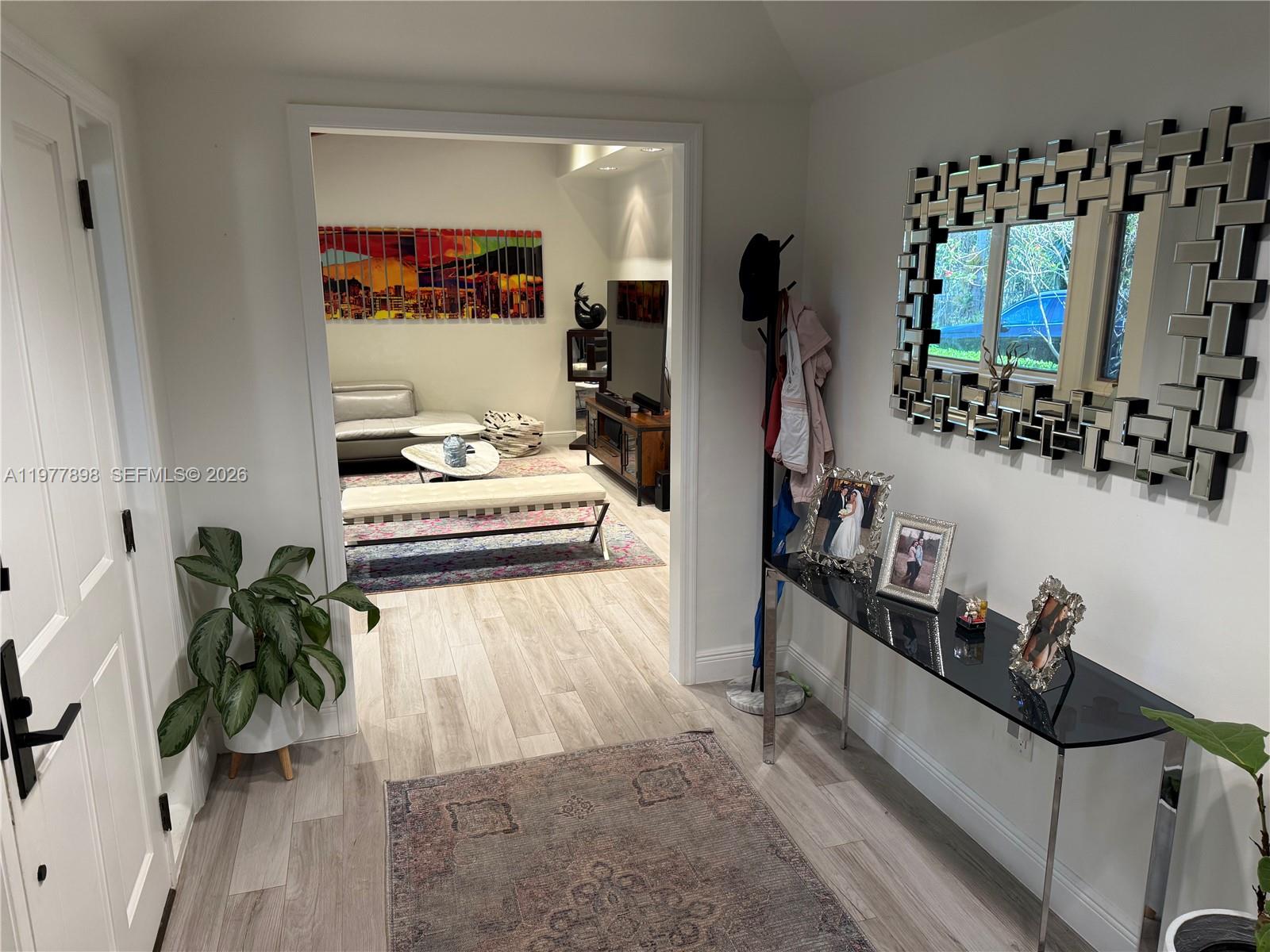 An entryway with a console table and mirror leads into a living room with wood flooring — 6399 SW 100th St # 0, Pinecrest FL 33156, PINECREST, FL