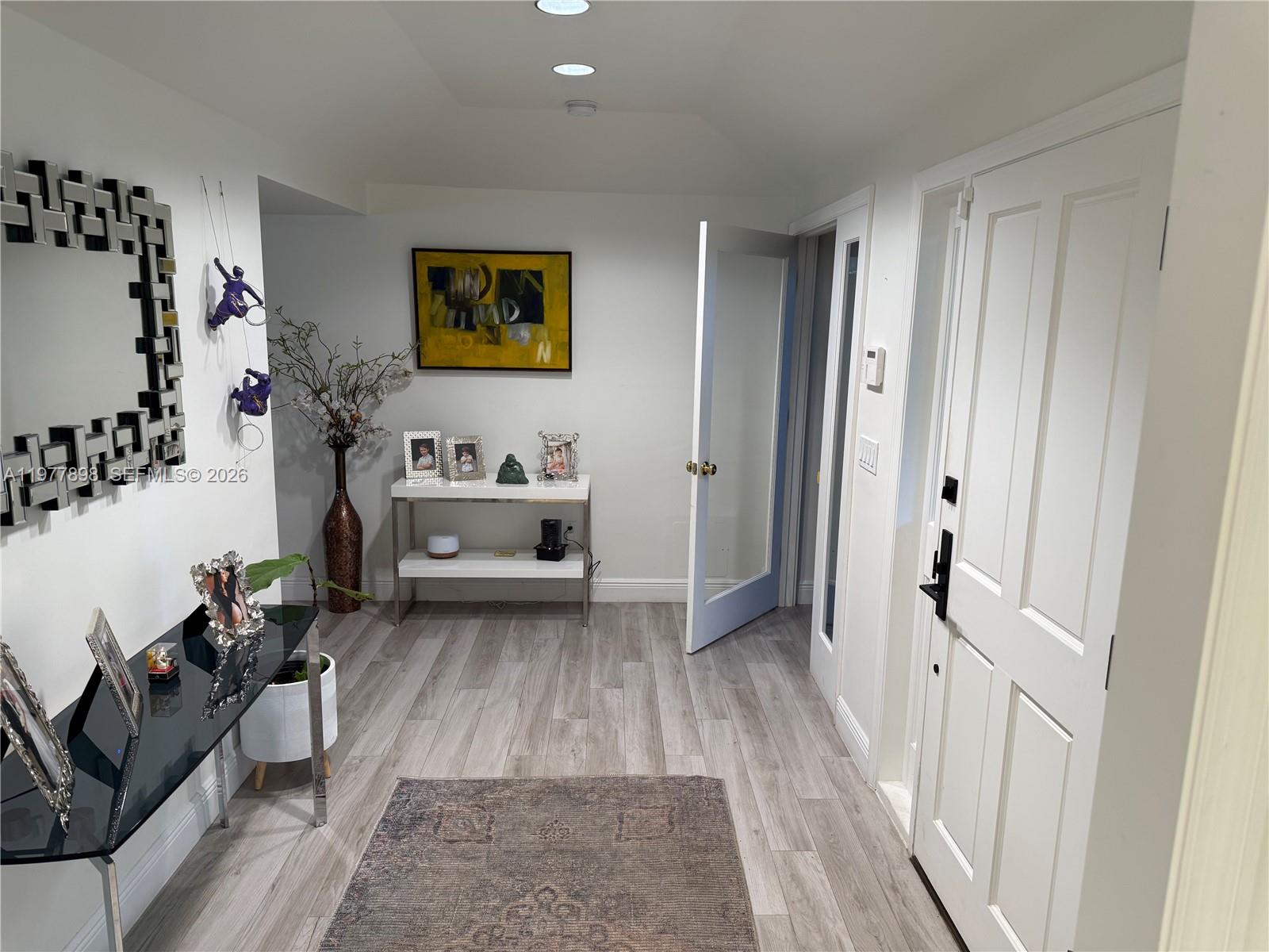 An entryway features light wood-look flooring, a black console table, and a white door — 6399 SW 100th St # 0, Pinecrest FL 33156, PINECREST, FL