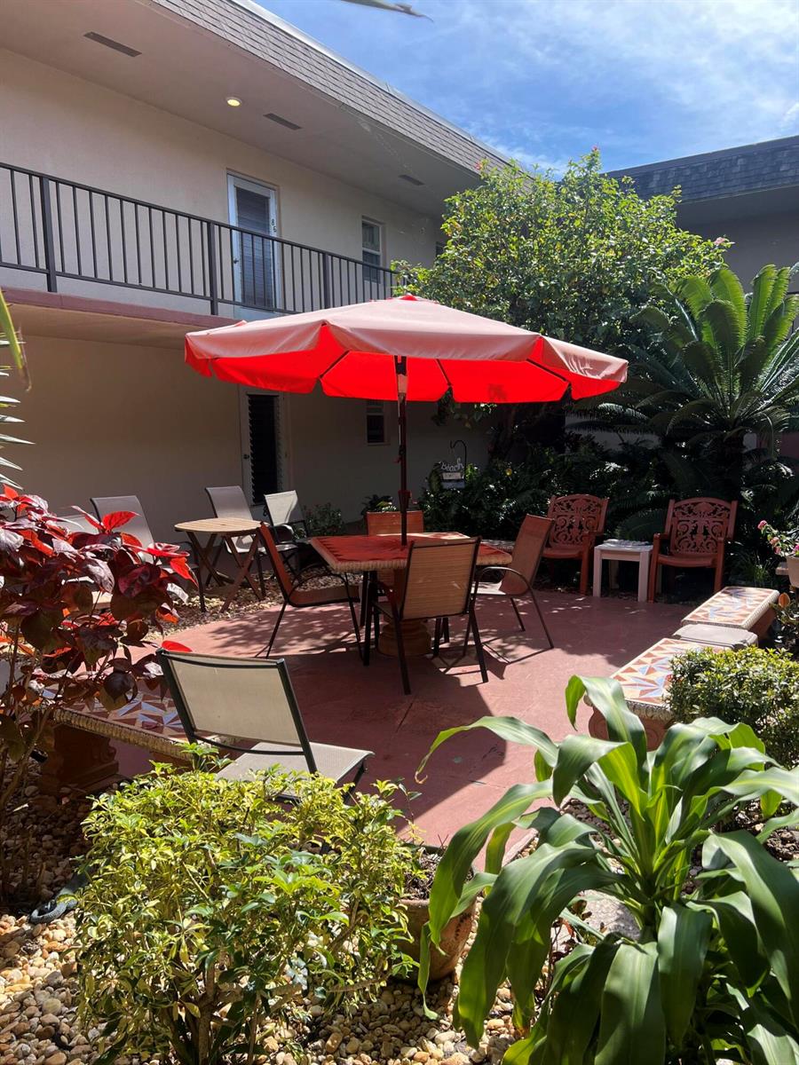 An outdoor patio area features a dining table with a red umbrella and surrounding chairs — 504 Davis Road # 95, Palm Springs FL 33461, PALM SPRINGS, FL