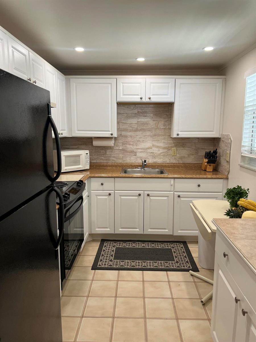 A kitchen features white cabinets, a tan countertop, a black refrigerator, and a tiled floor — 504 Davis Road # 95, Palm Springs FL 33461, PALM SPRINGS, FL