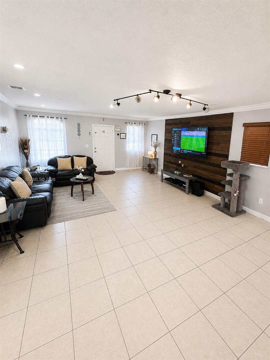 A living room features tile flooring, a wood-paneled accent wall with a television, and furniture — 7305 NW 173rd Dr # 102, Hialeah FL 33015, HIALEAH, FL