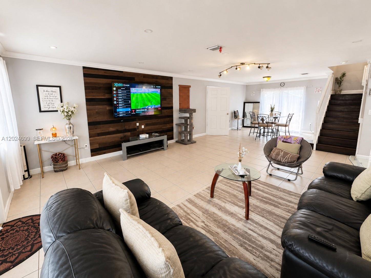 A living room features a wood-paneled accent wall, a wall-mounted television, and tile flooring — 7305 NW 173rd Dr # 102, Hialeah FL 33015, HIALEAH, FL