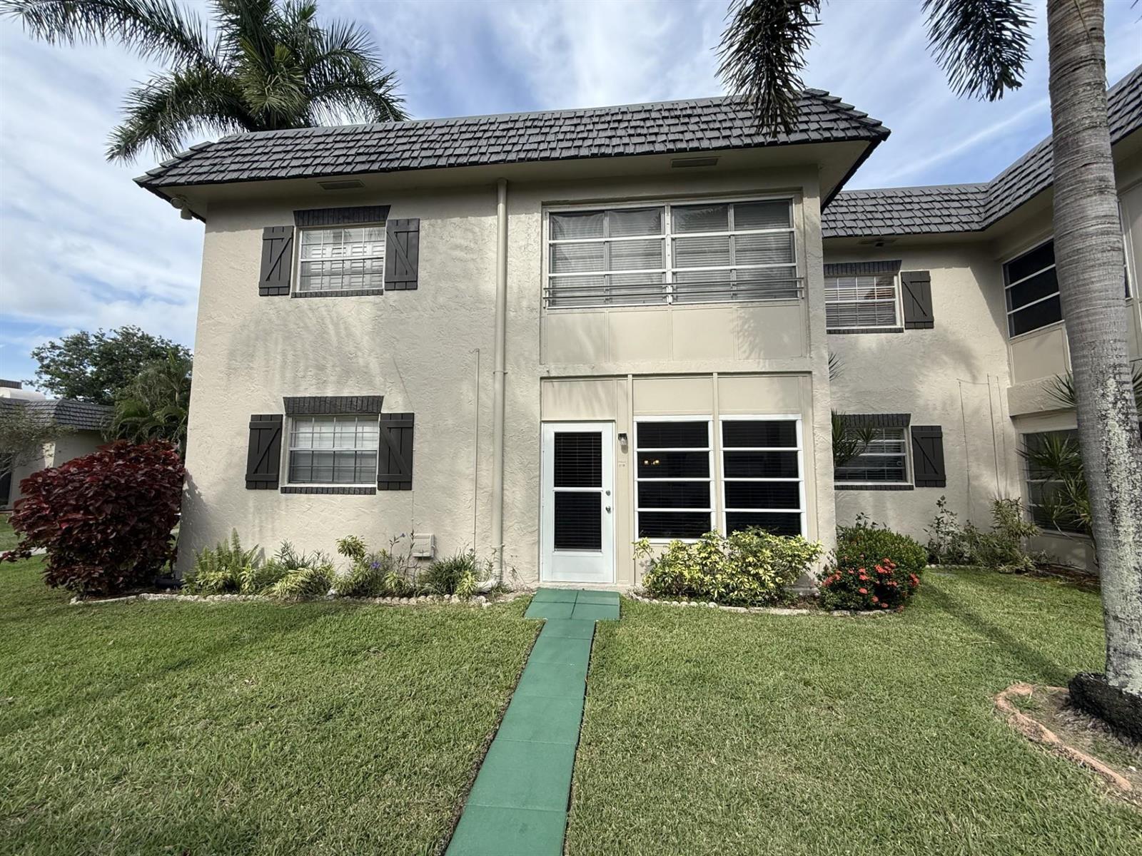 A two-story tan stucco townhouse with dark shutters, a green walkway, and palm trees — 375 SW 56th Avenue # 116, Margate FL 33068, MARGATE, FL