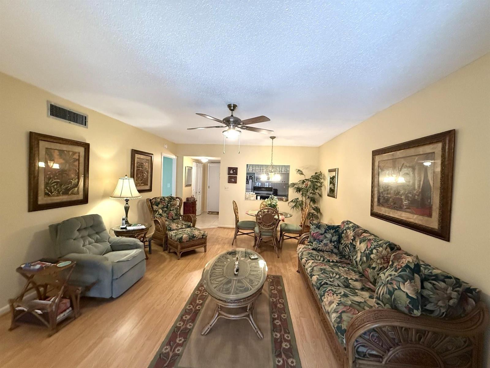 A living room with light wood floors, a floral sofa, and a dining area beyond — 375 SW 56th Avenue # 116, Margate FL 33068, MARGATE, FL