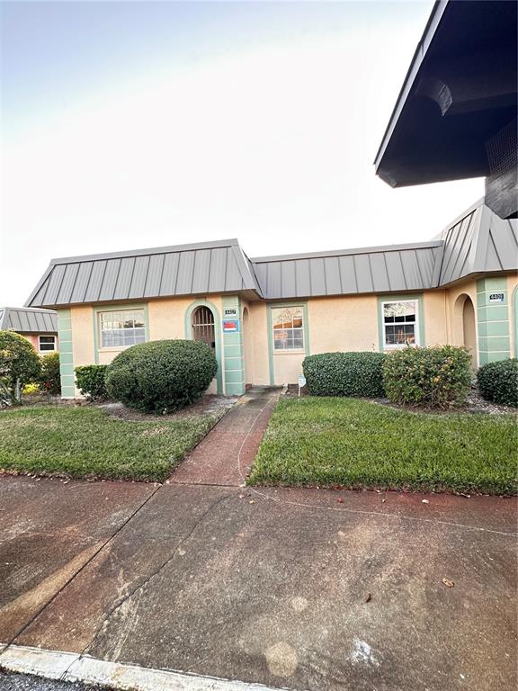 A single-story building with a metal mansard roof, stucco exterior, and a concrete walkway — 4407 SUMMERSUN DRIVE, NEW PORT RICHEY, FL