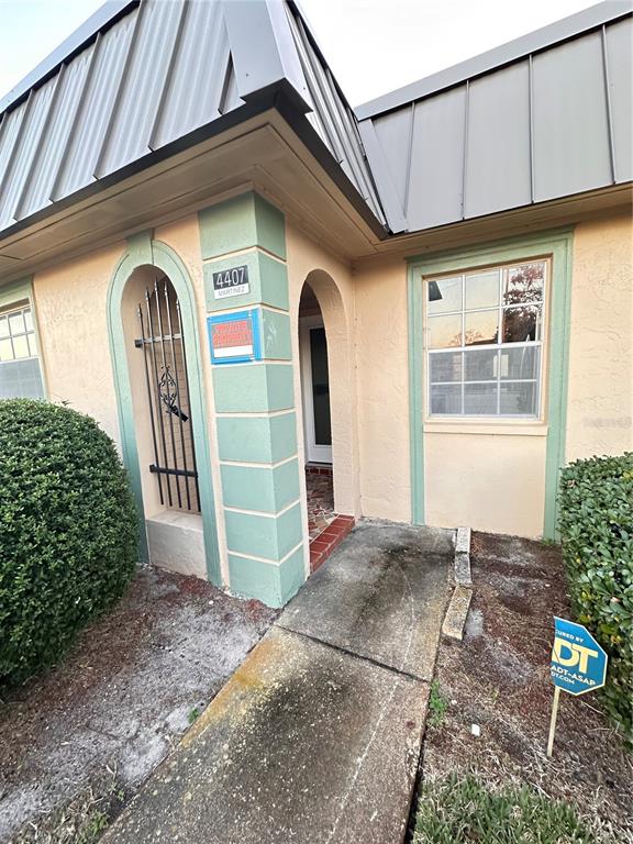 The exterior of a building features a tan stucco facade, a metal roof, and an entryway — 4407 SUMMERSUN DRIVE, NEW PORT RICHEY, FL