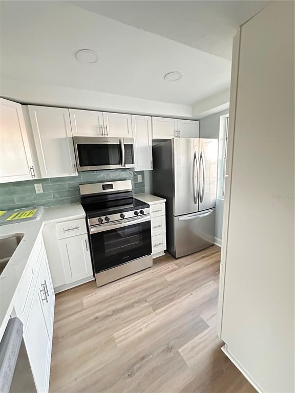 A kitchen features white cabinets, stainless steel appliances, a light green backsplash, and wood-look flooring — 4407 SUMMERSUN DRIVE, NEW PORT RICHEY, FL