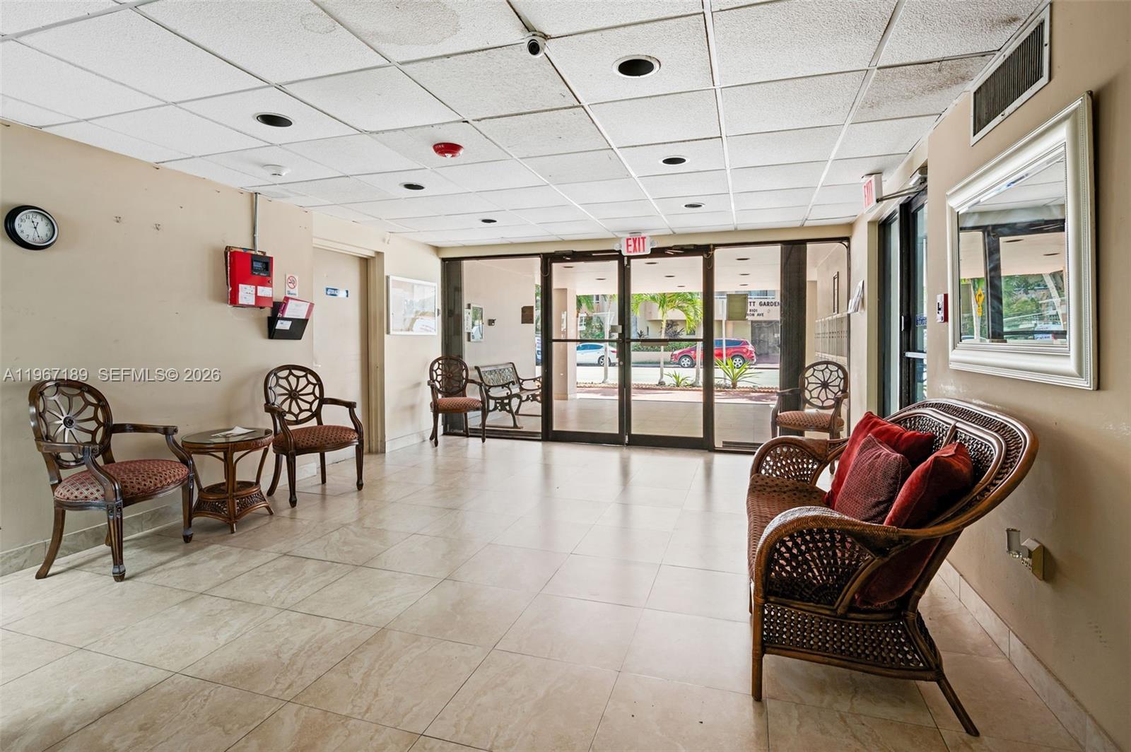 A lobby area features tile flooring, wicker furniture, a drop ceiling, and glass entrance doors — 8100 Byron Ave # 303, Miami Beach FL 33141, MIAMI BEACH, FL