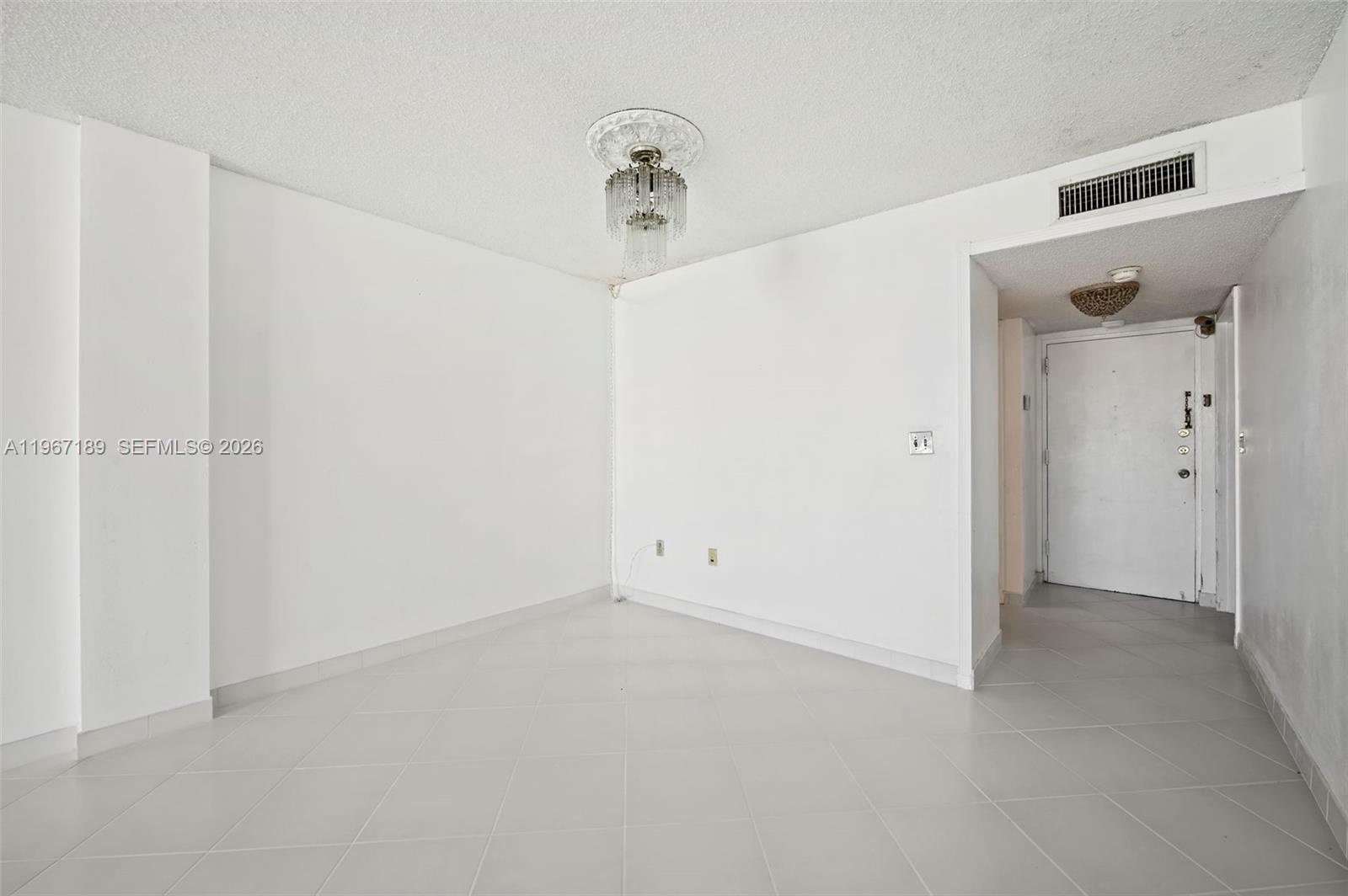 An empty room features white walls, light-colored tile flooring, and a crystal chandelier — 8100 Byron Ave # 303, Miami Beach FL 33141, MIAMI BEACH, FL