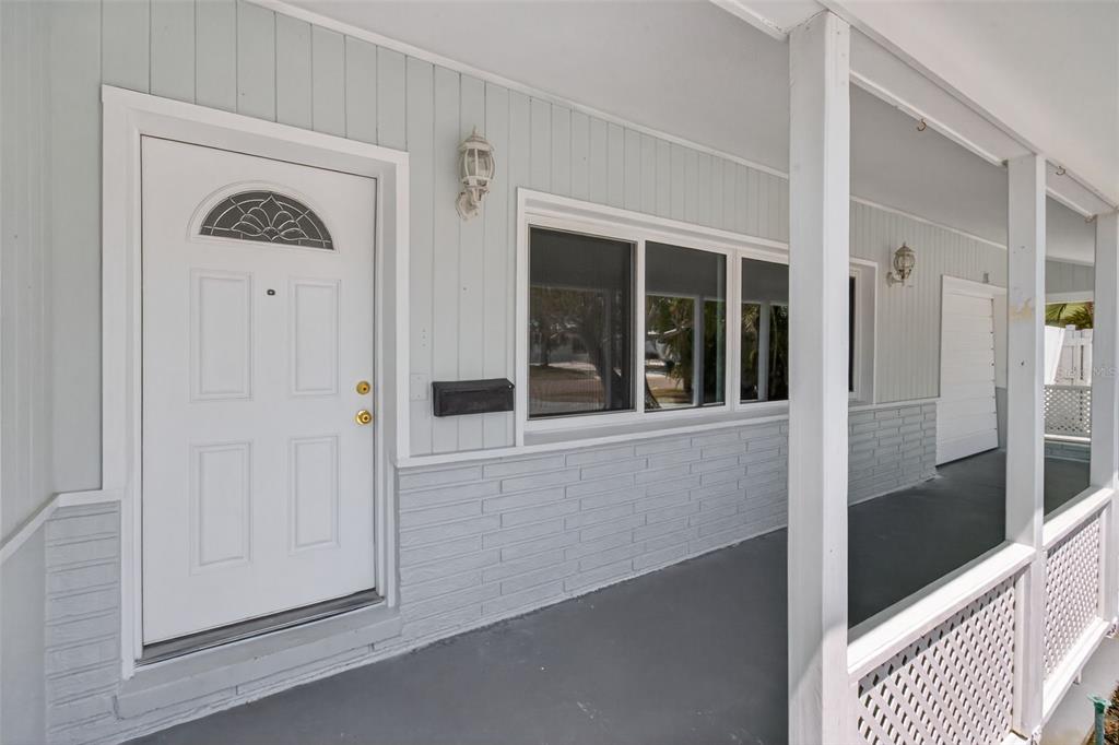 A covered porch features a white front door, light gray siding, and a brick base — 7919 CAUSEWAY BOULEVARD S, ST PETERSBURG, FL