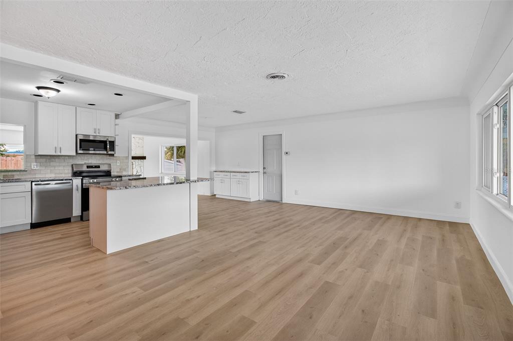 An open-concept kitchen and living area featuring white cabinetry, granite countertops, and wood-look flooring — 7919 CAUSEWAY BOULEVARD S, ST PETERSBURG, FL