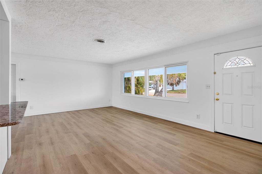 An empty living room with white walls, light wood-look flooring, and a front entry door — 7919 CAUSEWAY BOULEVARD S, ST PETERSBURG, FL