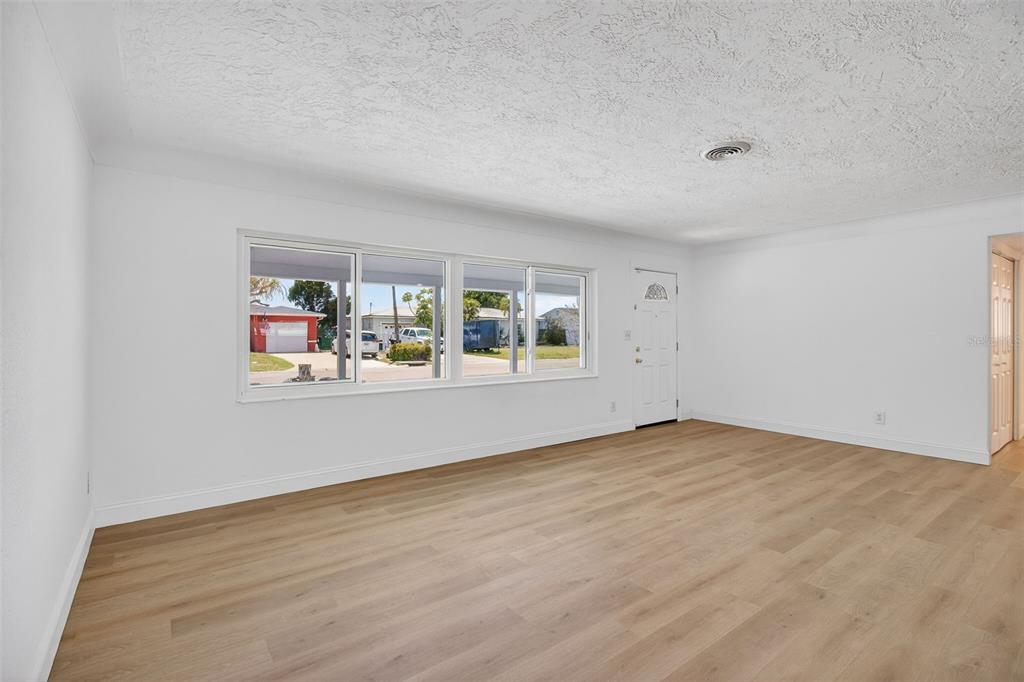 An empty living room with white walls, light wood-look flooring, and a large front window — 7919 CAUSEWAY BOULEVARD S, ST PETERSBURG, FL