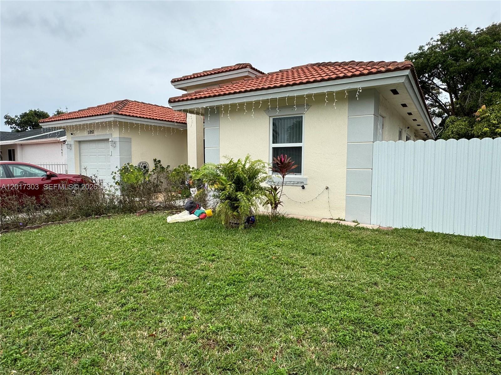 A single-story house with a red tile roof, beige stucco walls, and a white fence — 11951 SW 192nd Ter, Miami FL 33177, MIAMI, FL