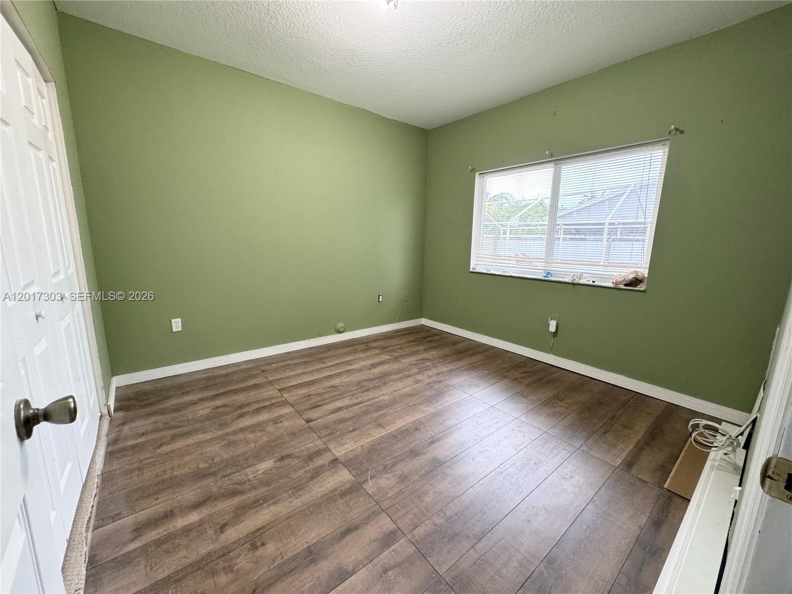 An empty bedroom features sage green walls, wood-look laminate flooring, and a single window — 11951 SW 192nd Ter, Miami FL 33177, MIAMI, FL