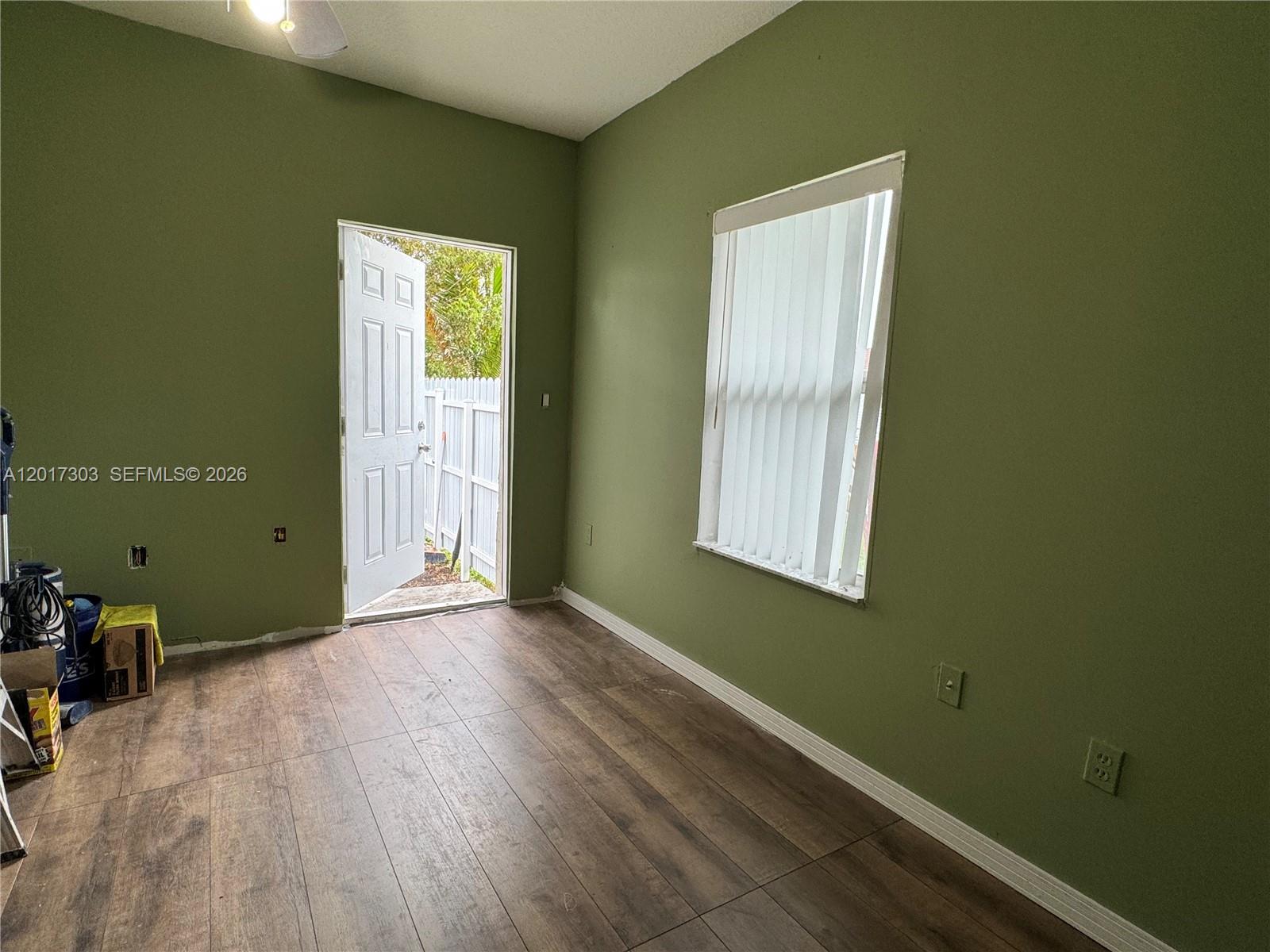 An empty room features sage green walls, wood-look flooring, a window, and an open door — 11951 SW 192nd Ter, Miami FL 33177, MIAMI, FL