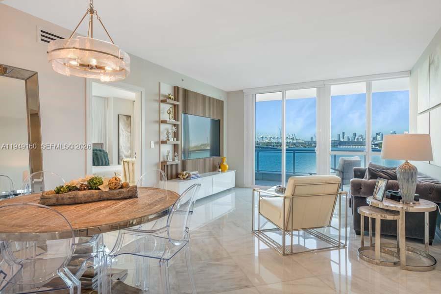 A bright living and dining area features marble floors, a wall-mounted television, and waterfront views — 540 West Ave # 411, Miami Beach FL 33139, MIAMI BEACH, FL