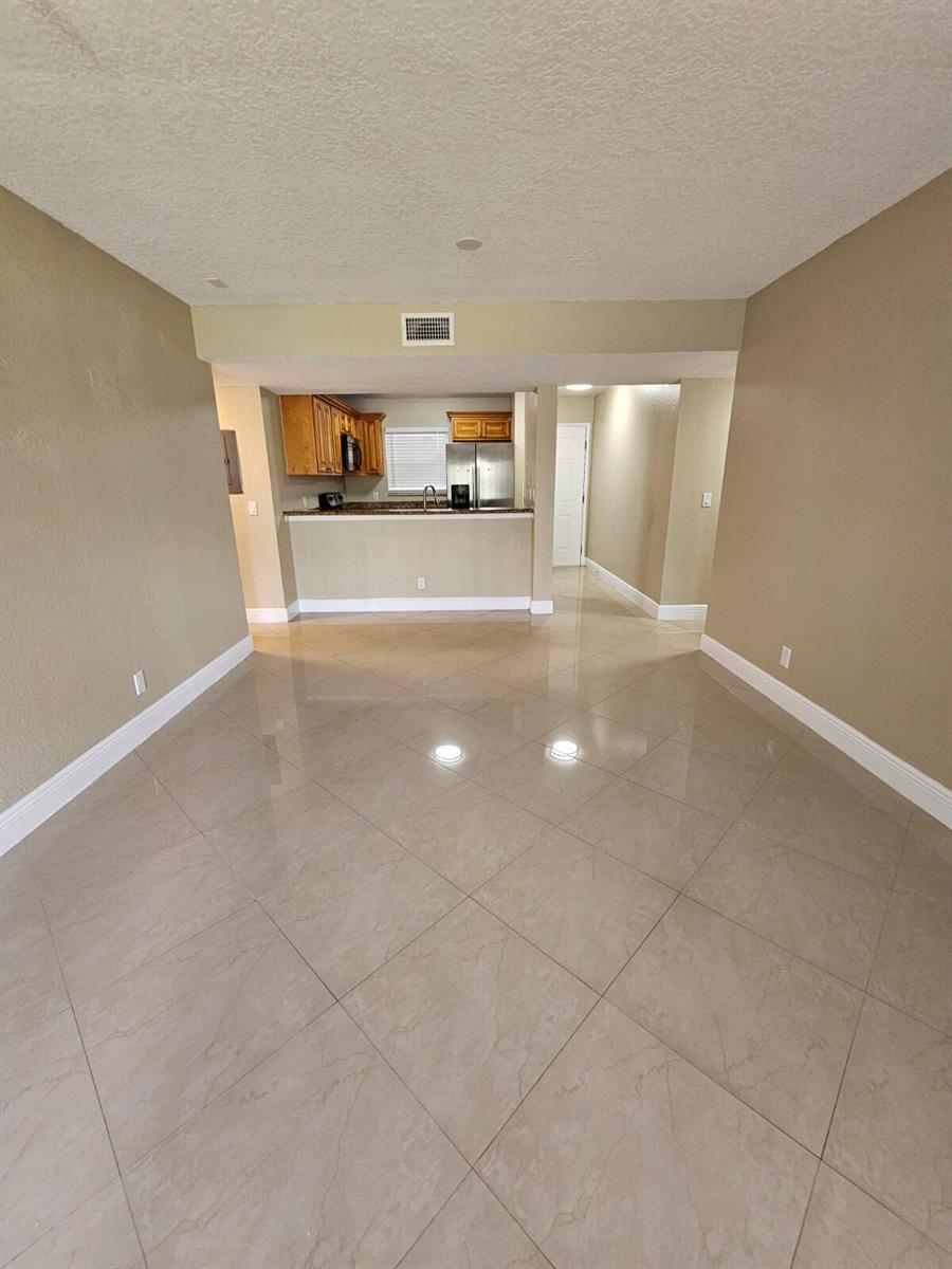 An open-concept living area features large beige floor tiles and a view into the kitchen — 1440 Windorah Way # C, West Palm Beach FL 33411, WEST PALM BEACH, FL