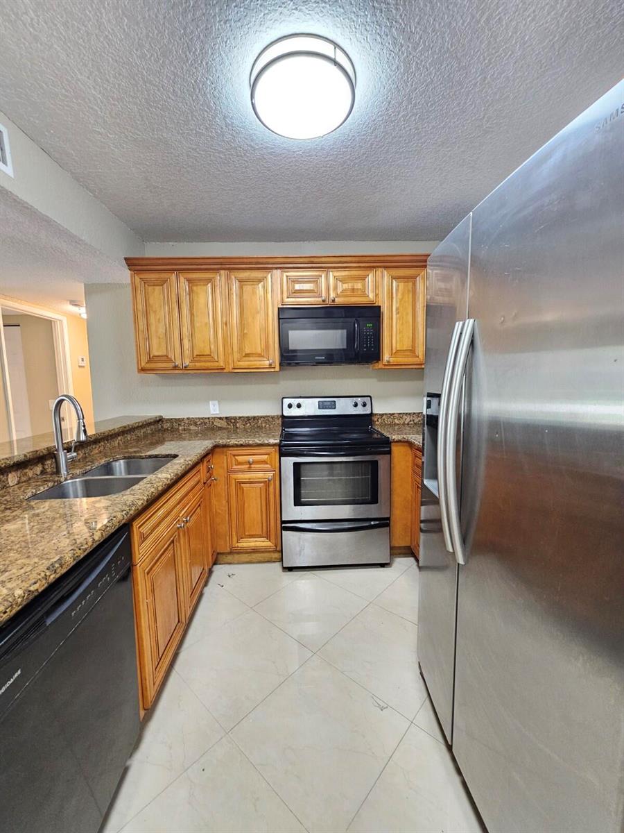 A kitchen features wood cabinets, granite countertops, stainless steel appliances, and light tile flooring — 1440 Windorah Way # C, West Palm Beach FL 33411, WEST PALM BEACH, FL
