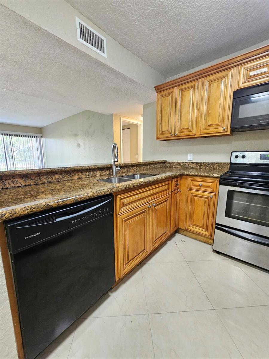 A kitchen features wood cabinets, granite countertops, stainless steel appliances, and a black dishwasher — 1440 Windorah Way # C, West Palm Beach FL 33411, WEST PALM BEACH, FL
